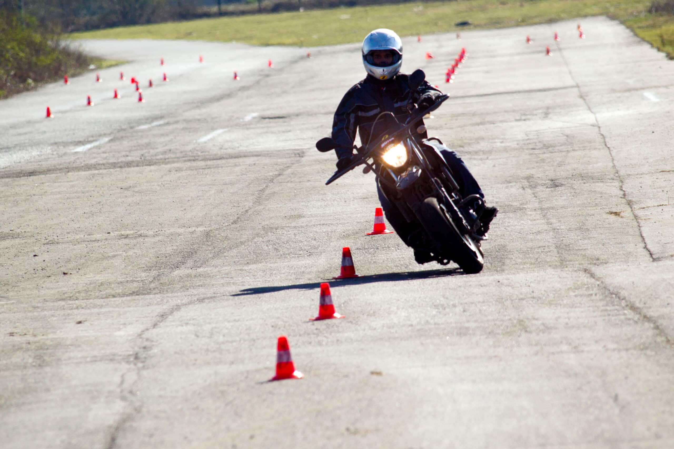 Motard en équipement de protection et casque argenté manœuvrant une moto sur un circuit d'entraînement délimité par des cônes oranges.